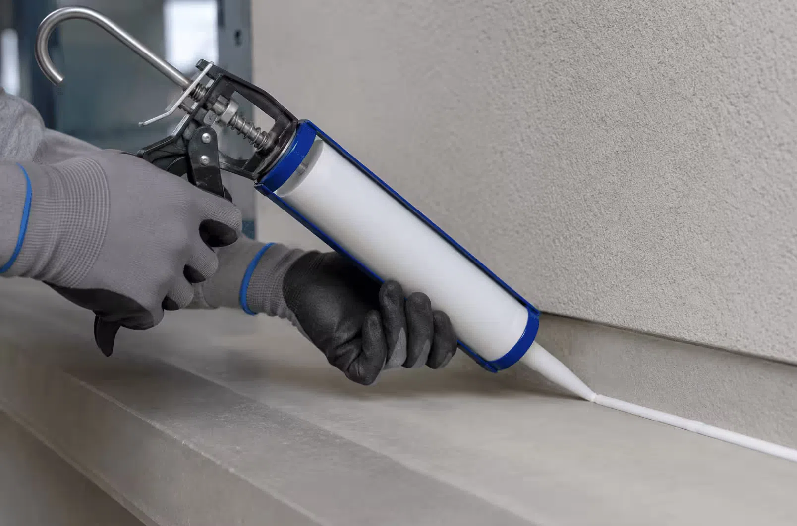 Pulling a manual caulking gun along a joint at a steady angle to keep the sealant bead even and prevent drip